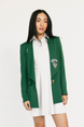 Woman wearing a green blazer with a logo over a white dress on a white background