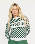 Woman wearing a green and white checkered Fore Sweater with 'FORE' text on a white background