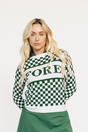 Woman wearing a green and white checkered Fore Sweater with 'FORE' text on a white background