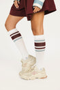 White knee-high socks with red and blue stripes worn with beige sneakers on a white background