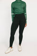 Person wearing a green long-sleeve top and black leggings on a white background