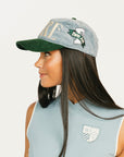 Woman wearing a blue and green cap with a logo, against a plain background