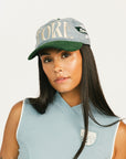 Woman wearing a cap and sleeveless top with branding on a plain background