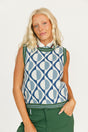 Woman wearing a patterned sleeveless sweater and green pants on a white background
