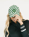 Person wearing a green and white checkered cap with a logo, against a plain background