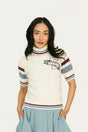 Woman wearing a Macbeth Turtleneck sweater, light blue skirt, and white sneakers on a white background