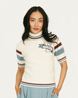 Woman wearing a striped sweater, light blue skirt, and white sneakers on a white background