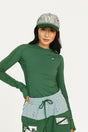Person wearing a green Marie long-sleeve shirt and light blue shorts with a cap on a white background