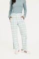 Person wearing a light blue long-sleeve top and plaid pants with white sneakers on a white background