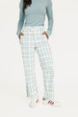 Person wearing a light blue long-sleeve top and plaid pants with white sneakers on a white background