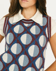Woman wearing a patterned sleeveless sweater over a white shirt with a plain background