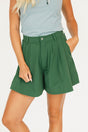 Person wearing a smoke blue sleeveless Annie Polo and a green Eleanor short on a plain background