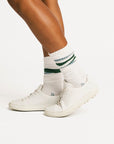 White sneakers with green accents worn with white socks on a light background