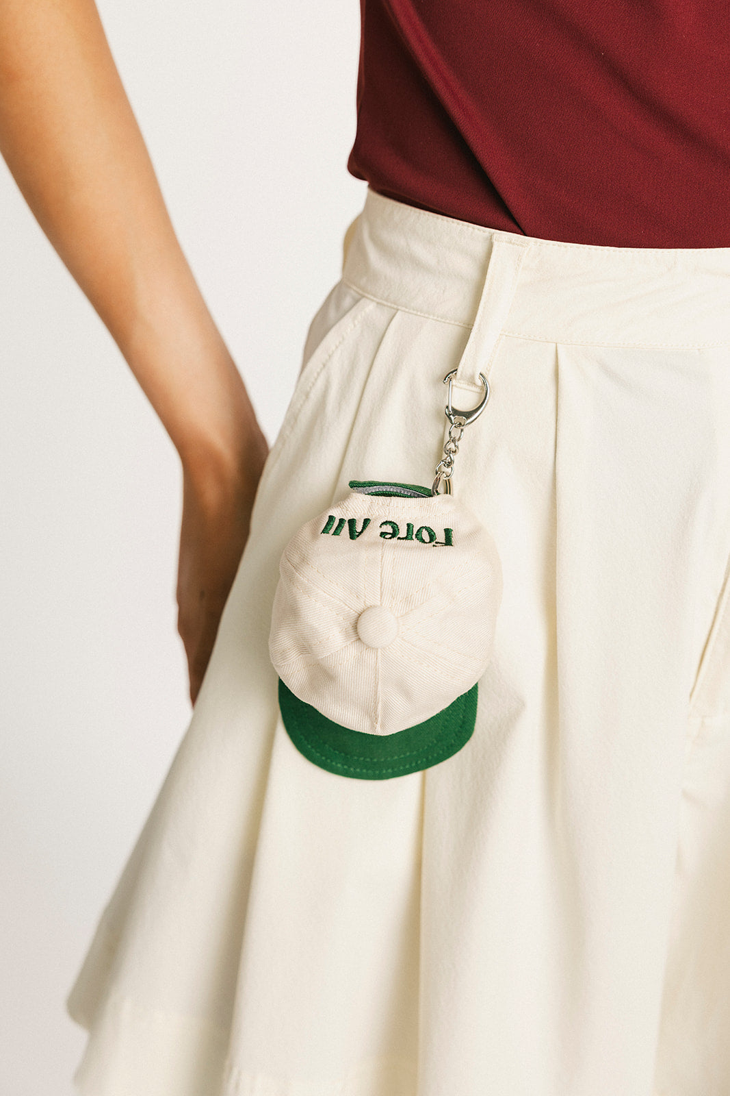 Person wearing a white cap with green brim and logo, held in front of a plain background