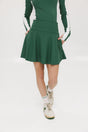 A person wearing a high-waisted green skirt with a solid pattern, paired with a white top and light-colored shoes.