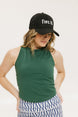 A woman wearing a green tank top with a built-in bra, paired with patterned shorts and a black cap with the text 'FORE ALL' on it.