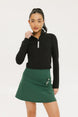 A woman wearing a black long-sleeve mock neck top with a green skirt. The top has a small logo on the neck area.