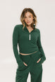 A woman wearing a green mock-neck long-sleeve golf top and matching pants, standing with hands in pockets.