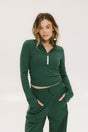 A woman wearing a green mock-neck long-sleeve golf top and matching pants, standing with hands in pockets.