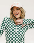 A female model wearing a green and white checkered golf top with long sleeves and a mock neckline.