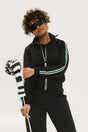 A person wearing a black jacket with green and white stripes on the sleeves, holding a black and white striped object.