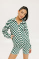 A woman is wearing a long sleeve jacket and shorts with a green and white checkered pattern.