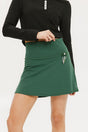 A person wearing a green golf skirt with side trim details, paired with a black long-sleeve top and sports footwear.