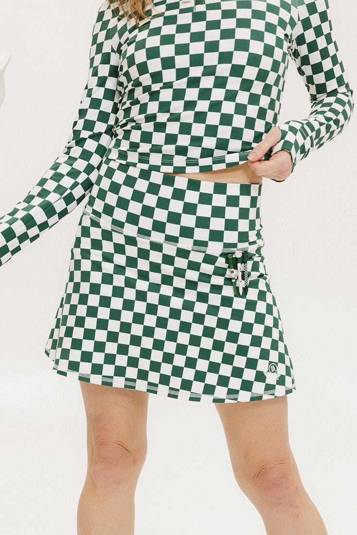 A person wearing a green and white checkered skirt with a matching long-sleeve top and sneakers, standing on a white background.
