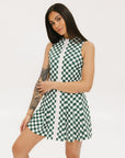 A model wearing a green and white checkered sleeveless dress with a zipper down the front and pockets.