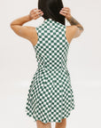 A model wearing a green and white checkered sleeveless dress with a zipper down the front and pockets.
