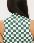 A model wearing a green and white checkered sleeveless dress with a zipper down the front and pockets.
