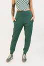 A pair of green athletic pants designed for golfing, with a comfortable waistband and a fitted design that enhances the silhouette. The pants are modeled by a woman who is also wearing a checkered top and sneakers.