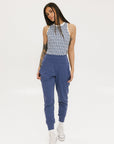 A female model wearing a sleeveless top with a geometric pattern and blue athletic pants, standing against a white background.