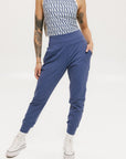 A female model wearing a sleeveless top with a geometric pattern and blue athletic pants, standing against a white background.