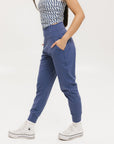 A female model wearing a sleeveless top with a geometric pattern and blue athletic pants, standing against a white background.