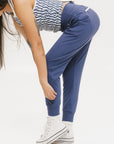 A female model wearing a sleeveless top with a geometric pattern and blue athletic pants, standing against a white background.