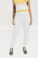 A person wearing white athletic pants and a white t-shirt with yellow details, standing against a white background.