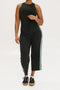 A female model wearing black sleeveless top and black crop pants with white side stripes, paired with black shoes.