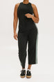 A female model wearing black sleeveless top and black crop pants with white side stripes, paired with black shoes.
