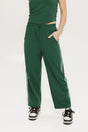 A person standing wearing green Bronson pants with a drawstring waist, green top, and black and white sneakers.