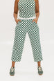 A pair of green checkered pants with a relaxed fit and pockets, worn by a model in a matching checkered top and sneakers.