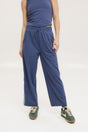 A person standing wearing indigo blue track pants with a drawstring waist and green sneakers.