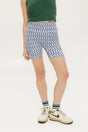 A pair of blue and white geometric shorts, knee-length, worn by a model paired with a green top and white sneakers.