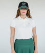 A woman wearing a white golf polo with a collar, a green skirt, and a black hat with text on it.