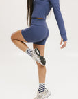 A person wearing indigo and white checkered Charlie Crew Socks with white sneakers and colorful pants.