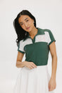 A woman wearing a color block green polo shirt with white front and back yoke detailing, paired with a white skirt.