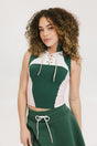 A female model wearing a sleeveless green and pink colorblocked mock neck top with mesh accents and a flat drawstring cord.