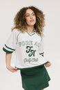 A woman wearing a white rugby-inspired polo shirt with green details and text that reads 'FORE ALL Golf Club'.