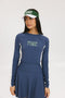 A female model wearing a long sleeve activewear top in blue and white with the text 'FORE' on the front, paired with a matching skirt and a visor with the text 'FORE'.