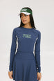 A female model wearing a long sleeve activewear top in blue and white with the text 'FORE' on the front, paired with a matching skirt and a visor with the text 'FORE'.